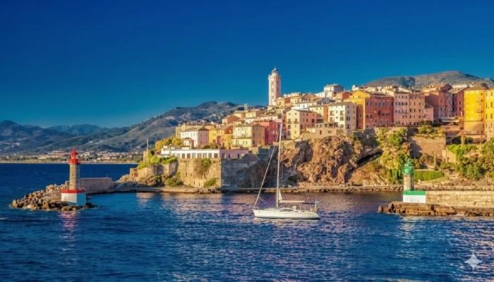 Maisons colorées et phare de Bastia illuminés par le soleil au bord de la Méditerranée.